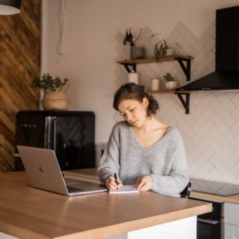busy female freelancer with laptop and notepad in kitchen